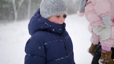 Ailesi olan bir çocuk kar altında tatilde kış ormanlarında yürüyor. Baba, anne, oğul ve kız Noel tatili için karlı bir günde dışarıda dinleniyorlar. Sıcak giysili insanlar. Yavaş çekim.