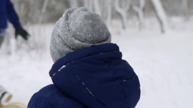 Karlı kış gününde mutlu aile kızakları. Anne ve baba, oğluyla kar yağarken kızak iplerini çekerler. Erkek dışarıda kızakla kayıyor. İnsanlar kızağa biniyor ve Noel tatilinin tadını çıkarıyor. Ağır çekim. Arka plan,