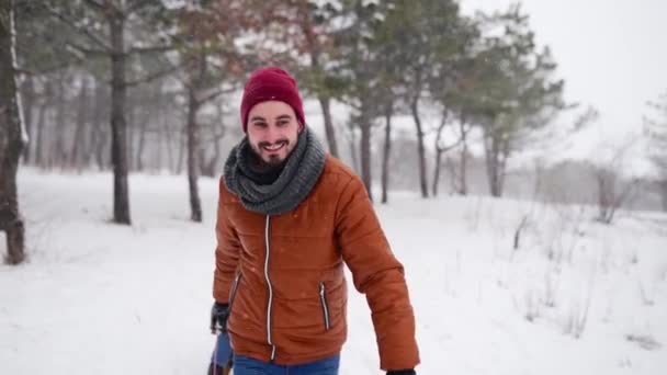 Härligt par pulka på snöig vinterdag. Man drar släde med flickvän på snöfall. Kvinna ha kul och släde utomhus med pojkvän. Människor släde rida och njuta av julen semester. Långsamma rörelser. — Stockvideo