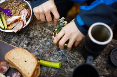 Yürüyüşçü orman kampında kahvaltı sırasında ahşap masadaki teneke kutuları açar. Ulusal parkta kamp yapan ve öğle yemeği yiyen insanlar. İzole görünüm