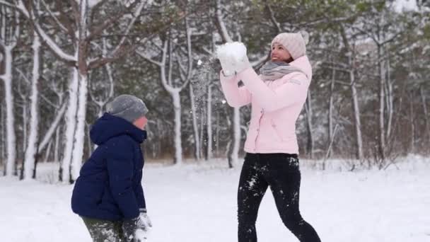 Boldog anya és fia játszani hóban, és dobja fel a levegőbe az erdőben a fagyos téli napon. Nő és fiú elegáns téli ruhát élvezze az első havas időjárás erdő parkban. Lassú mozgás.. — Stock videók