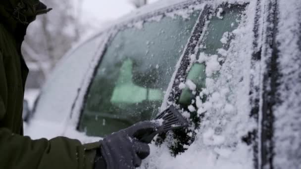 Pulizia dei finestrini laterali dell'auto con raschiaghiaccio prima del viaggio. L'uomo toglie il ghiaccio dai finestrini dell'auto. La mano maschile pulisce l'auto con uno strumento speciale durante la giornata invernale nevosa. Movimento lento 120 fps . — Video Stock