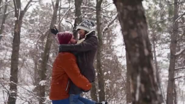 Férfi forog vagy fordul boldog barátnő tartja őt a kezében hóesés fenyőerdőben. Szerető pár érezd jól magad a havas téli parkban. Valentin nap és karácsony. Nő nevet lassított felvételen. — Stock videók