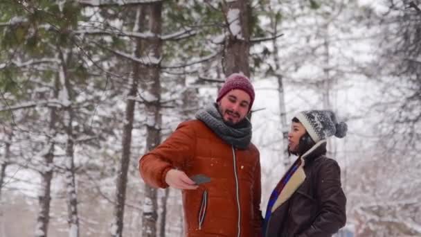 Молодая любящая пара хипстеров делает селфи под снегопадом в лесу. Блогер мужчина снимал на камеру смартфона с подругой для социальных сетей. Влиятельная семья наслаждается рождественскими каникулами . — стоковое видео
