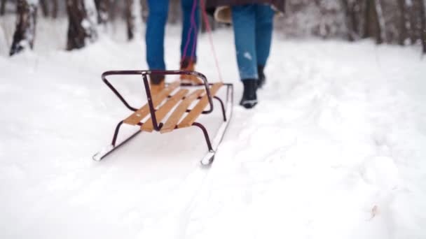 Achteraanzicht van mooie paar voeten wandelen slee trekken op besneeuwde winterdag. Man met vriendin gaat sleeën. Vrouw gaat buiten sleeën met vriendje. Mensen op kerstvakantie. Laaghoekschot. — Stockvideo