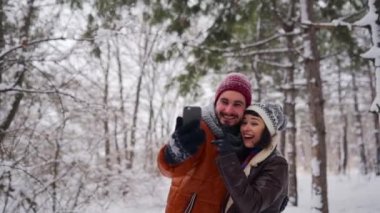 Genç aşık hipster çift ormanda kar altında sosyal medya için canlı yayın yapıyor. Kız arkadaşı görüntülü sohbette konuşan akıllı telefonlu blogcu adam. Etkilenen aile Noel tatilinin tadını çıkarıyor