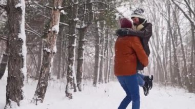 Dönen ya da mutlu bir kız arkadaşı döndüren bir adam çam ormanında kar yağışında onu elinde tutuyor. Sevgili çift, karlı kış parkında iyi eğlenceler. Sevgililer Günü ve Noel. Ağır çekimde gülen kadın.