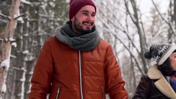 Jonge liefhebbende echtpaar wandelen in een park op sneeuw. Man en zijn vriendin die handen vasthouden en genieten van sneeuw op winterdag. Hipster vrouw wandeling in besneeuwd bos glimlachen met vriendje in stijlvolle kleding. — Stockvideo