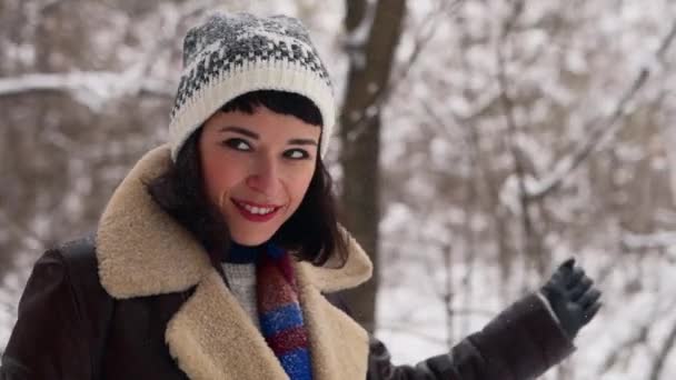 Hipster vrouw leunt haar hoofd op vriendjes schouder in besneeuwd bos. Jonge liefhebbende echtpaar in stijlvolle kleding wandelen in het park op sneeuw. Man en zijn vriendin genieten van sneeuw op winterdag. Slomo. — Stockvideo