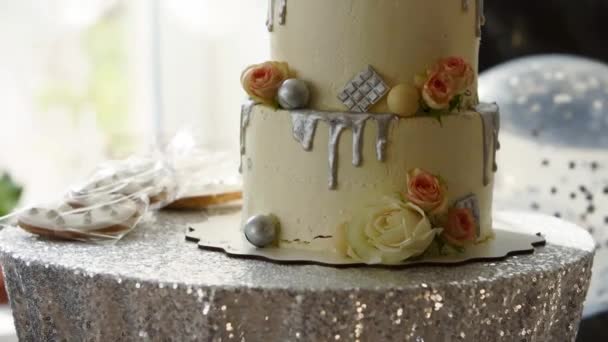 Γαμήλια τούρτα με τριαντάφυλλα, λευκό γλάσο και ασημένια επικάλυψη σε καραμέλα μπαρ. Γλυκά, μπισκότα και μπισκότα στο τραπέζι γενεθλίων. Μπαλόνια στο παρασκήνιο. — Αρχείο Βίντεο