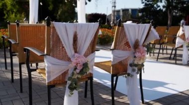 Güneşli yaz gününde çiçeklerle süslenmiş düğün yeri. Sandalyelerde çiçek süslemesi. Güller ve tüy otları, arka planda beyaz tekstil kemeriyle süslenmiş ampul çelenkleri..