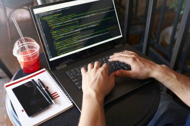 Dizüstü bilgisayarı olan bir geliştirici. Program kodu ve betik verileri ekranda. Gözlüklü genç serbest yazar kafede proje üzerinde çalışıyor. Omzundan geriye doğru bak.