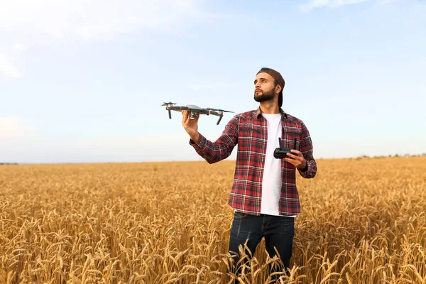 Vousatý hipster muž ukazuje malý kompaktní dron a drží dálkový ovladač v ruce. Zemědělský agronomista se dívá na quadcopter před vypuštěním na pšeničné pole — Stock fotografie