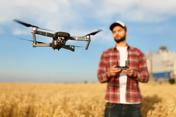 Un drone compact plane devant un agriculteur avec une télécommande dans ses mains. Quadcopter vole près du pilote. Agronomiste prenant des photos aériennes et des vidéos dans un champ de blé — Photo