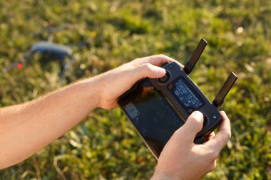 Adam uzaktan kumandayı elinde tutuyor. Quadcopter yere indi ve arka planda bulanık uçmaya hazır. Pilot motorları çalıştırıp havalanacak..