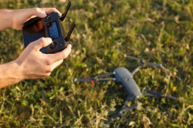 Adam uzaktan kumandayı elinde tutuyor. Quadcopter yere indi ve arka planda bulanık uçmaya hazır. Pilot motorları çalıştırıp havalanacak..