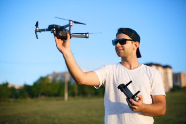 Mutlu gülümseyen adam elinde küçük bir dron ve uzaktan kumanda tutuyor. Pilot avucunun içinden kuadkopter fırlatır. İHA kalkışa hazır..