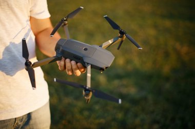 Adam küçük bir dron ve uzaktan kumanda gösteriyor. Pilot kuadkopteri elinde tutuyor.