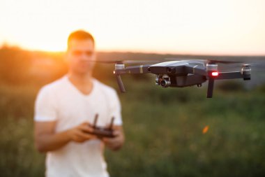 Drone elinde uzaktan kumandayla bir adamın önünde süzülüyor. Çeyrek helikopter pilotun yanında uçuyor. Yukarıdan havadan fotoğraf ve video çeken adam.