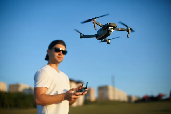 Compact drone hovers in front of man with remote controller in his hands. Quadcopter flies near pilot. Guy taking aerial photos and videos from above — Stock Photo, Image