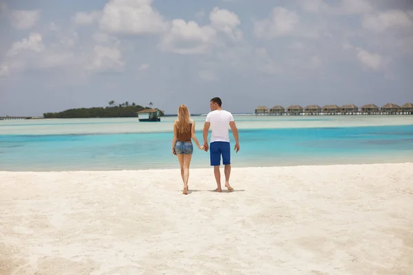 Vista traseira do casal de mãos dadas e caminhando até a lagoa azul do oceano em Maldivas no resort de spa de luxo. Viagens e conceito de lua de mel . — Fotografia de Stock