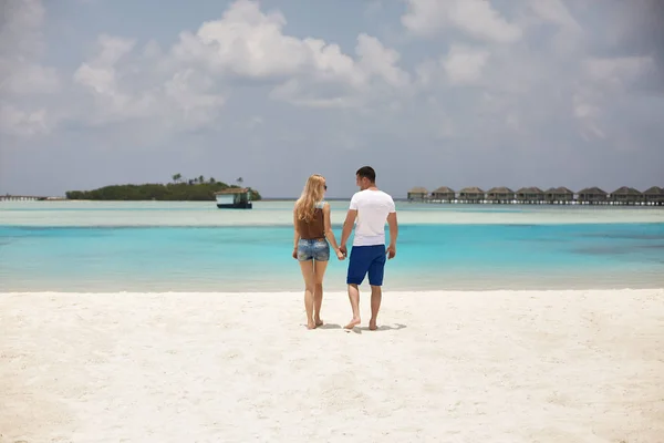Vista traseira do casal de mãos dadas e caminhando até a lagoa azul do oceano em Maldivas no resort de spa de luxo. Viagens e conceito de lua de mel . — Fotografia de Stock