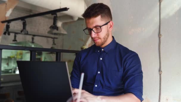 Joven hipster freelancer atractivo trabajando remotamente en el ordenador portátil en la cafetería loft. Empresario navegando por internet en Coffeshop. Blogger publica en las redes sociales sobre viajes usando internet 5g. Tema Telecommuting . — Vídeos de Stock