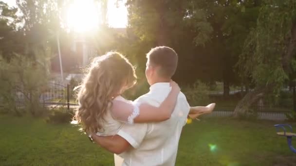 Pan młody kręci się ze szczęśliwą panną młodą na rękach. Nowożeńcy bawią się w ciepły letni dzień ślubu na świeżym powietrzu. — Wideo stockowe
