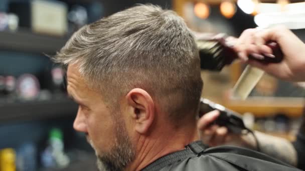 Barber woman cuts bearded mans hair with a clipper in barbershop. Mens hairstyling and hair cutting in salon. Grooming the hair with trimmer. Hairdresser doing haircut in retro hair salon. — Stock Video