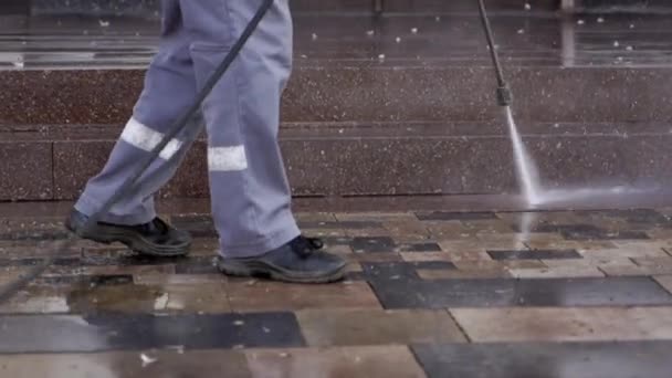 Limpieza de calles de la ciudad con lavadora a presión de agua. El conserje rocía la acera de la ciudad pavimentando losas. El trabajador desinfecta el suelo y las superficies del coronavirus. Medidas sanitarias antibacterianas en cuarentena — Vídeo de stock