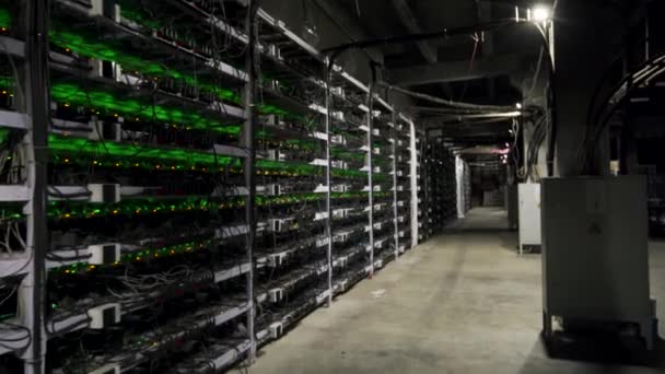 Cryptocurrency mining equipment on large farm. ASIC miners on stand racks mine bitcoin in server room. Blockchain techology application specific integrated circuit. Steadycam footage along racks. — Stock Video