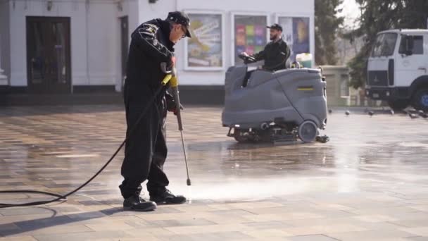 12 de marzo de 2020 - Mariupol, Ucrania. Barredora de calles coche limpieza acera de la ciudad pavimentación de losas con lavadoras a presión y escobas giratorias al aire libre. Detalles de la máquina de barrido de carreteras . — Vídeo de stock