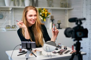 Güzellik blogcusu kadın tripodla kameranın yanında günlük makyaj rutin dersini çekiyor. Etkilenen sarışın kız ev stüdyosunda canlı yayın yapan kozmetik ürünleri incelemesi yapıyor. Ruj karşılaştıran bir kadın..
