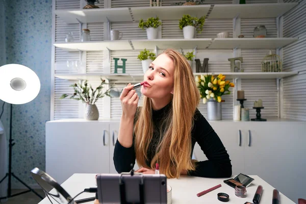 Vlogger female applies lipstick on lips. Beauty blogger woman filming daily make-up routine tutorial at camera on tripod. Influencer blonde girl live streaming cosmetics product review in home studio — Stock Photo, Image