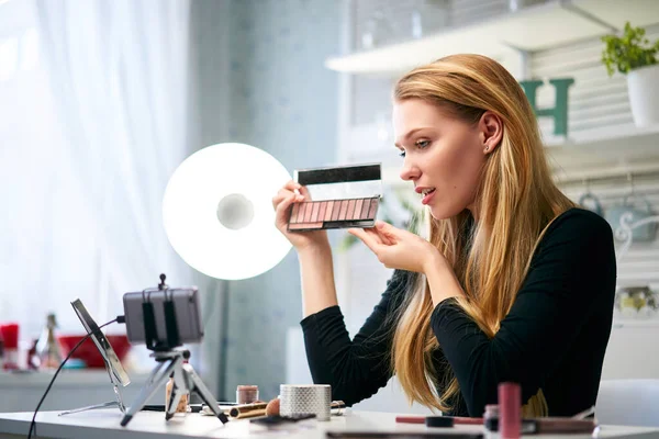 Vlogger female showing eye shadow palette. Beauty blogger woman filming daily make-up routine tutorial near camera on tripod. Influencer girl live streaming cosmetics product review in home studio. — Stock Photo, Image