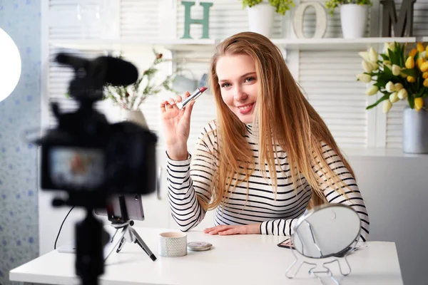 Vlogger kvinna visar läppstift. Skönhetsbloggare kvinna filmar dagliga make-up rutin handledning nära kameran på stativ. Influencer blond flicka live streaming kosmetika produktrecension i hemstudio — Stockfoto