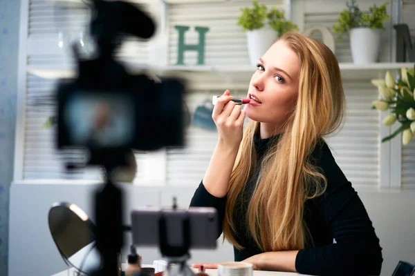 Vlogger female applies lipstick on lips. Beauty blogger woman filming daily make-up routine tutorial at camera on tripod. Influencer blonde girl live streaming cosmetics product review in home studio — Stock Photo, Image