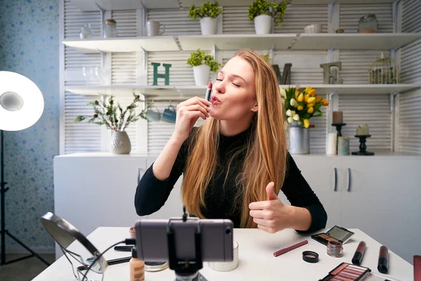 Vlogger female applies lipstick on lips. Beauty blogger woman filming daily make-up routine tutorial at camera on tripod. Influencer blonde girl live streaming cosmetics product review in home studio — Stock Photo, Image