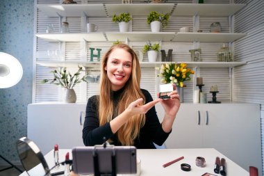 Güzellik blogcusu kadın kameranın yanında günlük makyaj rutin çekimleri yapıyor. Etkilenen kız canlı yayın kozmetik ürünleri incelemesi yapıyor. Vlogger dişisi göz farı paleti öneriyor..