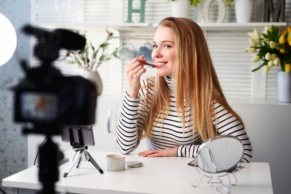 Vlogger female applies lipstick on lips. Beauty blogger woman filming daily make-up routine tutorial at camera on tripod. Influencer blonde girl live streaming cosmetics product review in home studio — Stock Photo, Image