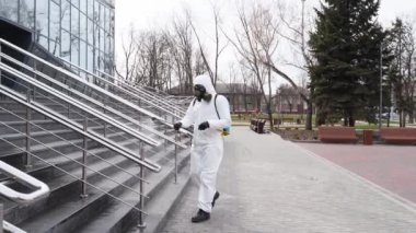 Antibakteriyel spreyle koronavirüs covid-19 karantinasının tırabzan dezenfekte yüzeyini dezenfekte eder. Gaz maskeli ve koruyucu giysili işçiler şehrin kamusal alanındaki tırabzanları temizliyor..