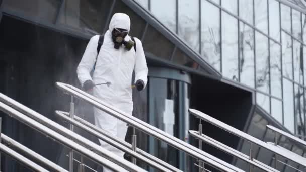Sanitizer disinfects railing touch surfaces on coronavirus covid-19 quarantine with antibacterial sprayer. Worker in gas mask and hazmat protective suit cleans handrails in city public place. — Stock Video