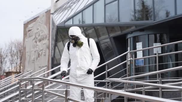 Sanitizer desinfecteert railing touch oppervlakken op coronavirus covid-19 quarantaine met antibacteriële sproeier. Werknemer in gasmasker en hazmat beschermend pak reinigt leuningen in de stad openbare plaats. — Stockvideo