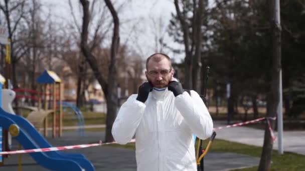 Le préposé à l'enlèvement des matières dangereuses porte une combinaison de protection contre les nattes dangereuses et un masque facial avec du matériel d'assainissement posé pendant l'éclosion du virus. Hero shot de l'homme en respirateur avec pulvérisateur. Coronavirus, COVID-19 — Video