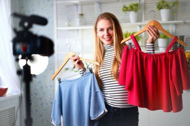 Kot pantolon ve balıkçı yaka giyen moda blogcusu kadın kamerada sıradan renkli gömlekler gösteriyor. Stilist kız, kendi kanalı için son moda kıyafetleri gösteren video bloğu bölümünü çekiyor. Fikir lideri eğilimleri belirler.