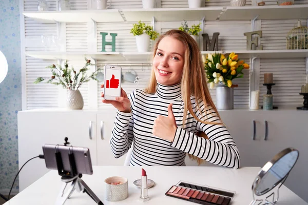 Skönhet bloggare kvinna filma reklam och hålla smartphone ber om gillar, tummen upp, prenumeration på kameran. Makeup influencer blond flicka live streaming kosmetika produktrecension i studio. — Stockfoto