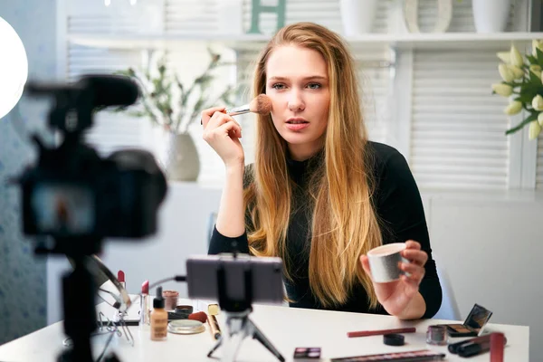 Güzellik blogcusu kadın tripodla kameraya günlük makyaj dersini çekiyor. Etkilenen kız canlı yayın kozmetik ürünleri eleştirisi ev stüdyosunda. Vlogger dişisi fırçayla cilt pudrası uyguluyor. — Stok fotoğraf