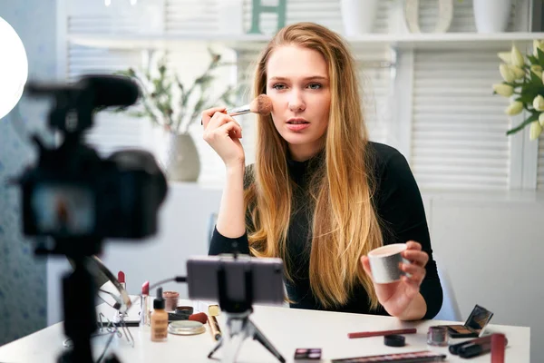 Beauty blogger woman filming daily make-up routine tutorial at camera on tripod. Influencer girl live streaming cosmetics product review in home studio. Vlogger female applies skin powder with brush. — Stock Photo, Image