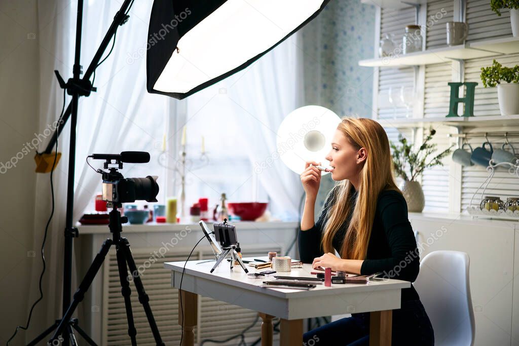 Beauty blogger woman filming daily make-up routine tutorial on camera. Influencer blonde girl live streaming cosmetics product review in home studio with professional lighting equipment. Vlogger job.