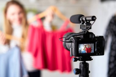 Kot pantolon ve balıkçı yaka giyen moda blogcusu kadın kamerada sıradan renkli gömlekler gösteriyor. Stilist kız, kendi kanalı için son moda kıyafetleri gösteren video bloğu bölümünü çekiyor. Fikir lideri eğilimleri belirler.